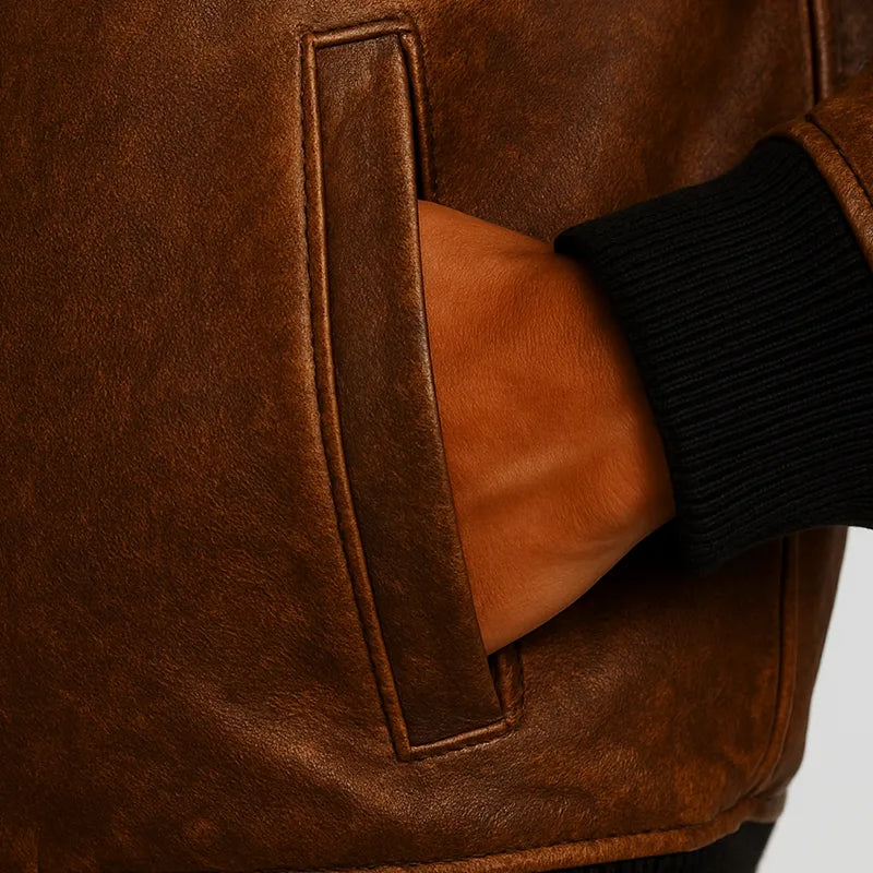 Close-up of a brown leather jacket with a pocket, showing a black sleeve.