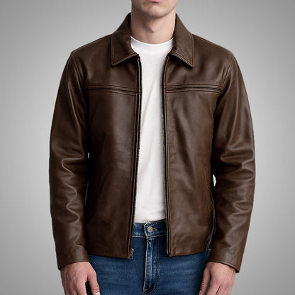 Man wearing a brown leather jacket over a white shirt and blue jeans on a gray background